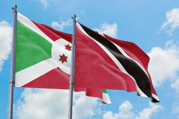 Trinidad And Tobago and Burundi flags waving in the wind against white cloudy blue sky together. Diplomacy concept, international relations.