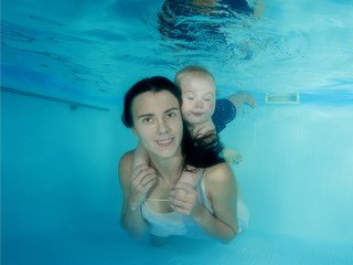Mom with a little son dives underwater in a swimming pool
