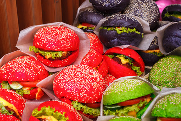 Black, red and green colored burgers are lying on a market counter