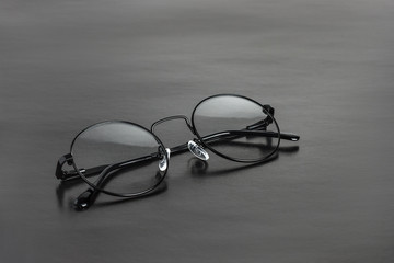 The round black metal medical eye glasses with folded temples on a black background