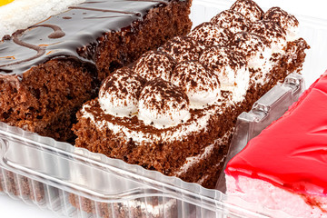 Assorted Tiramisu cakes in transparent plastic box on white background close-up