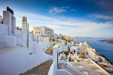 Fira town on Santorini island, Greece. Traditional and famous houses and churches with blue domes over the Caldera, Aegean sea. Terraces of Santorini hotels in the morning light. - obrazy, fototapety, plakaty