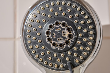 Close-up of an old used silver and grey colored shower head with limescales in the bathroom in front of white tiles