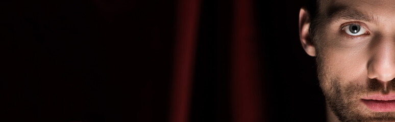 panoramic shot of young magician in black suit in circus with red curtains