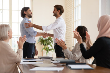 Smiling businessman shake hand of male newcomer at meeting