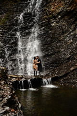 Fototapeta na wymiar vacation in norway, couple in love passionate kiss near a waterfall, rocks and mountains,
