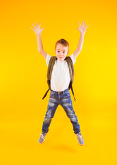 Happy child jumping with backpack over yellow background back to school