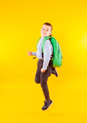 Full length photo of small pupil jump high. Happy schoolboy with backpack isolated on yellow background.