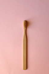 Bamboo toothbrush on pale pink background. Zero waste lifestyle concept. Flat lay.