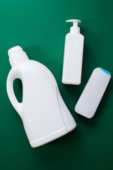 Plastic bottles of cleaning products over green background. Top view. Flat lay.