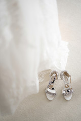 White shoes of the bride in brilliant crystals stand next to the dress. Things for an elegant wedding.