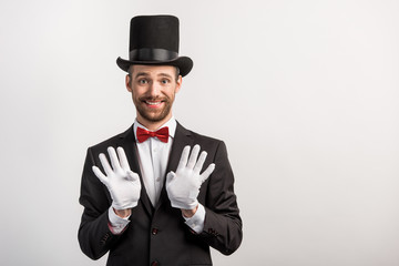cheerful handsome magician in gloves gesturing, isolated on grey