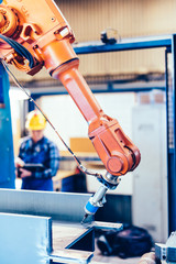 Worker operating robotic arm to cut steel in a factory.