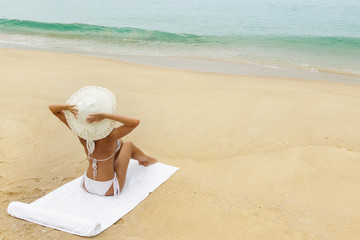 Fototapeta na wymiar Woman in hat sitting on the beach