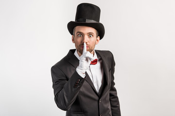 surprised magician in gloves showing silence symbol, isolated on grey
