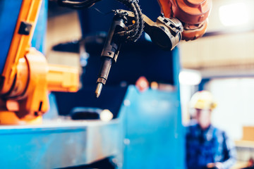 Worker operating robotic arm to cut steel in a factory.