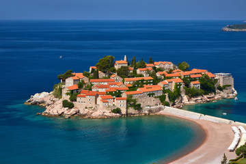 Amaizing sunset view on Sveti Stefan Island City. Small islet and resort in Montenegro. Balkans, Adriatic sea, Europe. Sunny day on the beach near the Saint Stefan island. Bridge on the old town.