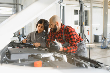 Auto car repair service center. Mechanic examining car engine. Female Mechanic working in her workshop. Auto Service Business Concept. Pro Car female Mechanic Taking Care of Vehicle.