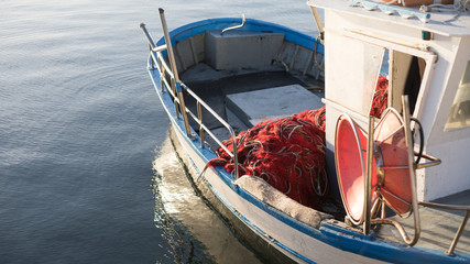 The moored fishing boat is lulled by the water while the sun reflects on the sea early in the morning with the winch of the fishing net in the foreground