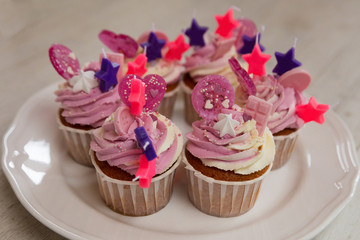 Tasty cupcakes for birthday party with stars decorations on a white wooden table. Cakes decorated with cheese cream, candies and chocolate.