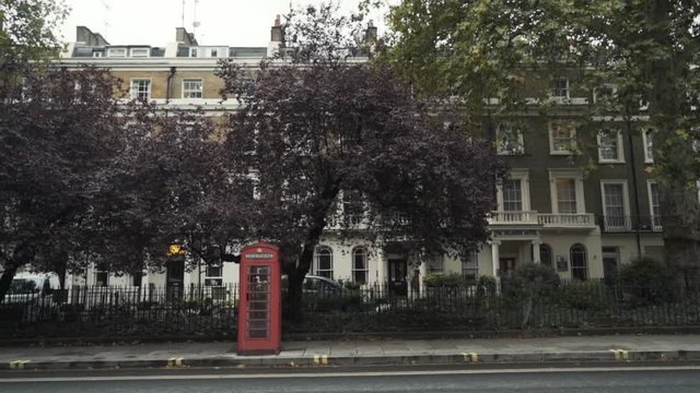 Traditional red telephone boxes in London standing on the street near the road against the trees. National symbols of England