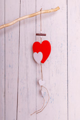 A red romantic wooden heart hanging on painted white boards. Hearts handing on the rope. Valentine's day greeting card. Love concept