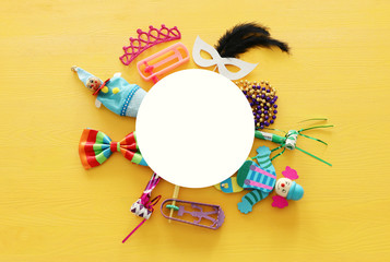 Party colorful noisemaker, mask and cute clown doll over yellow wooden background . Top view, flat lay