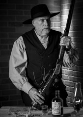 1885 old west cowboy standing in a saloon holding his rifle wide shot