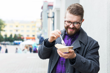 Fast food and meal concept - Young man eating take away food on the street