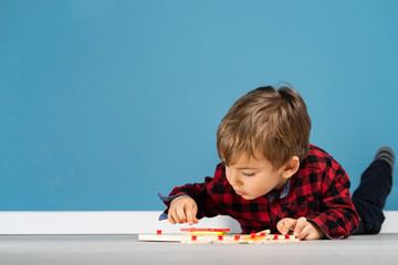Portrait of small little caucasian boy young child kid laying in front of the blue wall background wearing red and black shirt in studio playing with puzzle toy at home