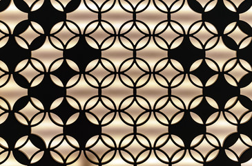 Fototapeta premium Decorative metal lattice with interior backlight. Black lattice on a beige background.