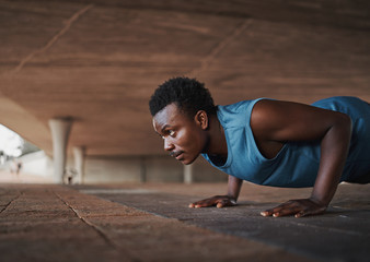 Fototapeta na wymiar Determined young african american male athlete training in city, doing push ups on pavement in morning