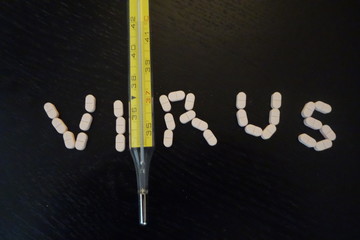 Medical concept: pills forming the word virus and thermometer on black background