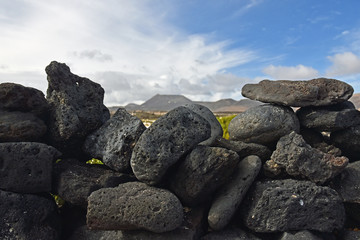 Volcanic stone wall with blurred volcano in background, Lanzarote, Spain