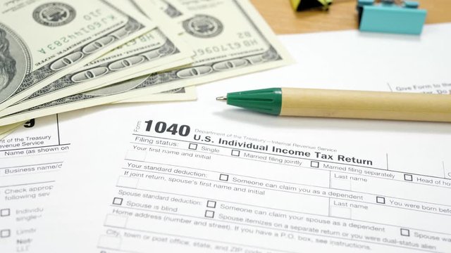 U.S. Dollar Banknotes and 1040 Tax Form. Binder Clips with Money and Green Pen. Individual Income Tax Return. Tax Payment Concept. Filing Taxes Document