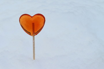 Red heart shaped lollipop sticks out of snow in winter