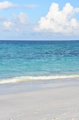 Sandy tropical beach and blue turquoise ocean water under blue sky