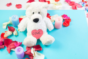 On a blue background in rose petals, a teddy bear with a heart and the inscription love.