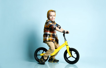 Fototapeta na wymiar Boy in bright stylish casual clothing, sneakers, cap and round sunglasses standing near yellow run bike present