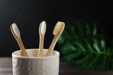 Close-up of a white ceramic glass with three biodegradable bamboo toothbrushes on a dark...