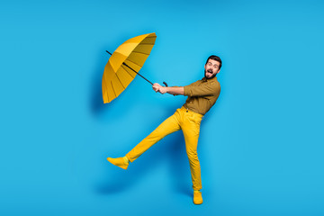 Omg parasol flying. Full size photo of crazy astonished man catch his rain wind protect shield umbrella scream wear plaid pants sneakers isolated over blue shine color background