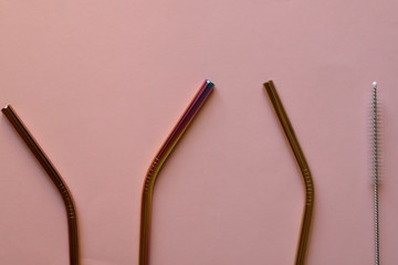 Reusable metal straws and cleaner, on pale pink background. Flat lay.