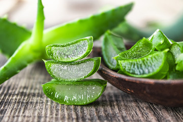 Fresh aloe vera leaves and slices of aloe vera in a spoon on a wooden background.