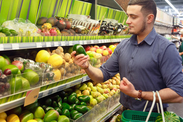 Young man customer choosing avocados in supermarket