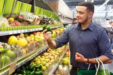 Young man customer choosing avocados in supermarket