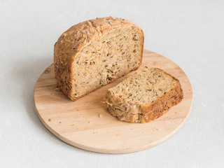 Half a loaf of homemade whole grain bread with various seeds and two slices on a white background