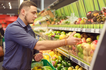 Man in a supermarket at the shelf for fruits shopping for groceries, he is checking out the apples.