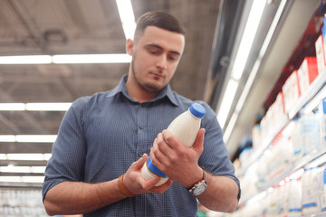 A man read bottle with milk or yogurt in the milk department of the supermarket. A man buys dairy products in the store