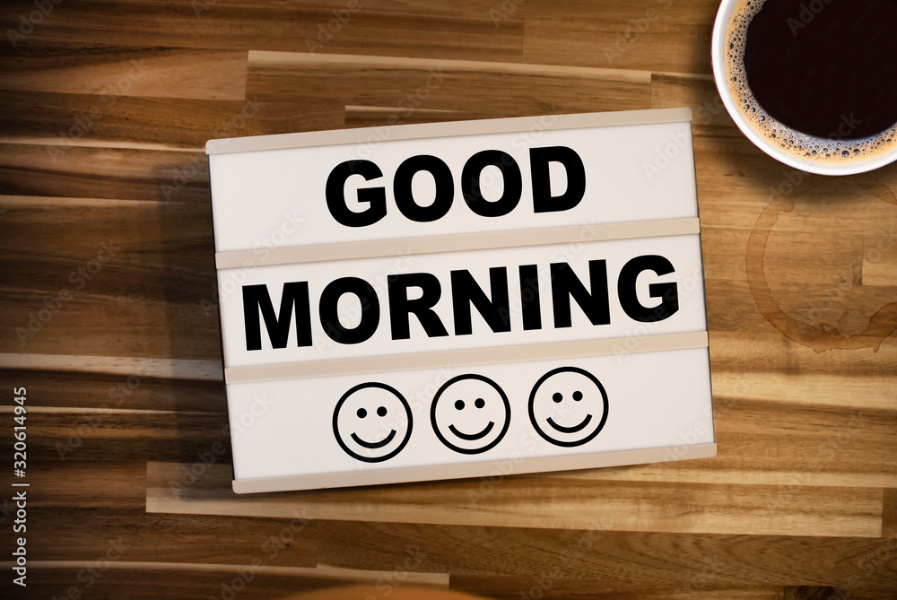 Wall mural lightbox or light box with happy faces and message good morning on a wooden table with a cup of coff