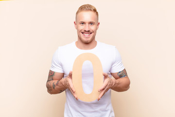 young blonde man excited, happy, joyful, holding a number 0.